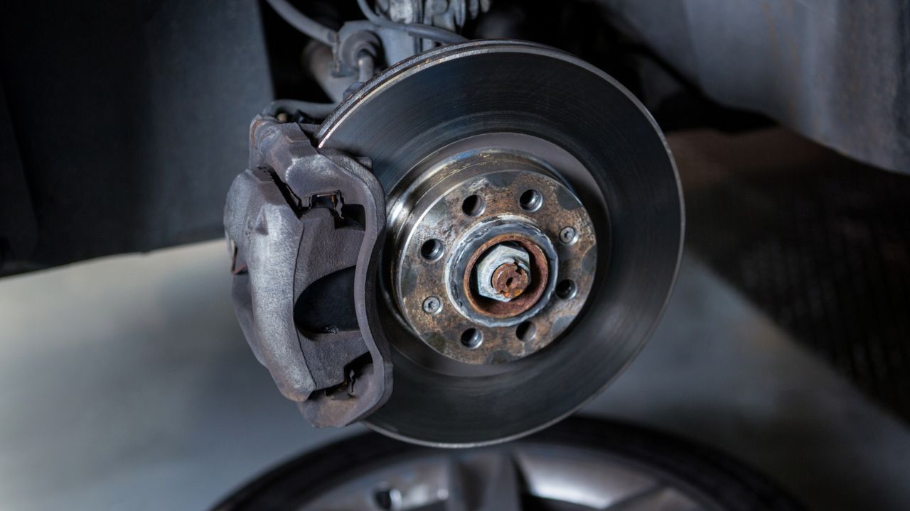 Close-up of a car’s brake rotor and caliper with surface rust around the wheel hub.