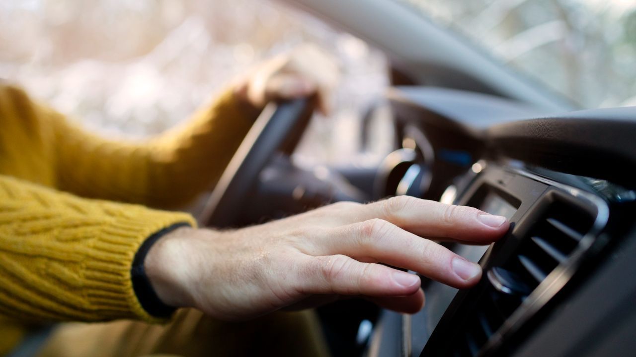 Driver adjusting the air vent and climate control dials on a car center console while driving
