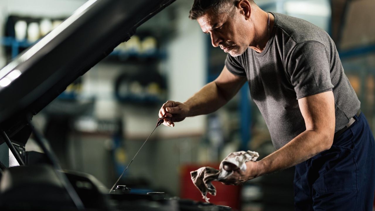 Mechanic checking engine oil with a dipstick during a routine vehicle maintenance inspection.