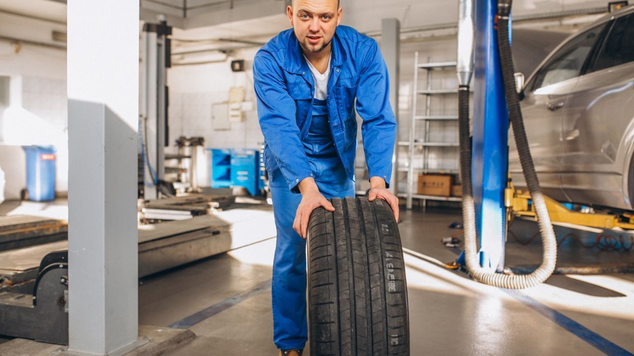 Mechanic rolling a replacement tire through an automotive repair shop