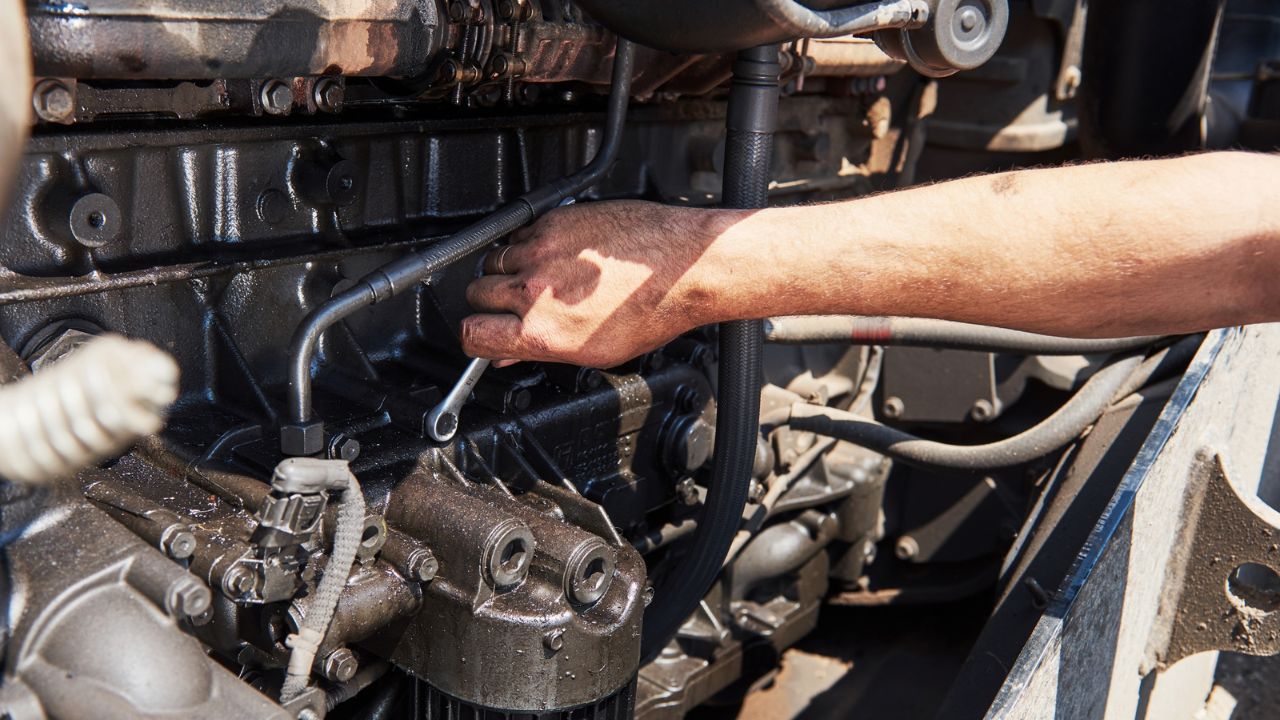 Technician repairing a vehicle engine with hand tools during professional engine diagnostics and repair service.