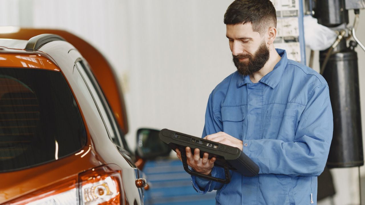 Professional auto technician using a diagnostic tablet while inspecting a vehicle during routine maintenance and safety checks.