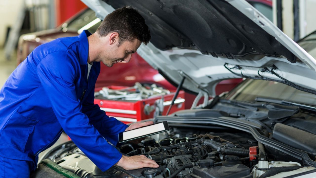 : Mechanic using a diagnostic tablet to inspect a car engine under the hood
