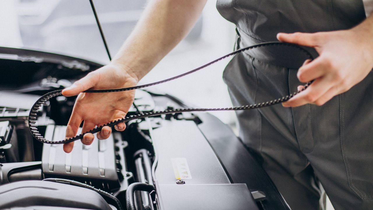 Mechanic holding a toothed timing belt above an open car engine bay.