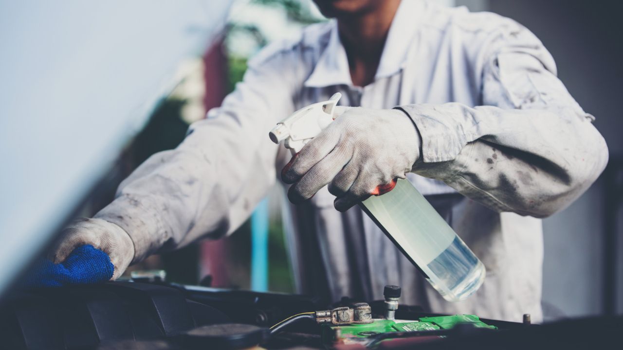 Auto technician cleaning vehicle engine components with spray cleaner and microfiber cloth
