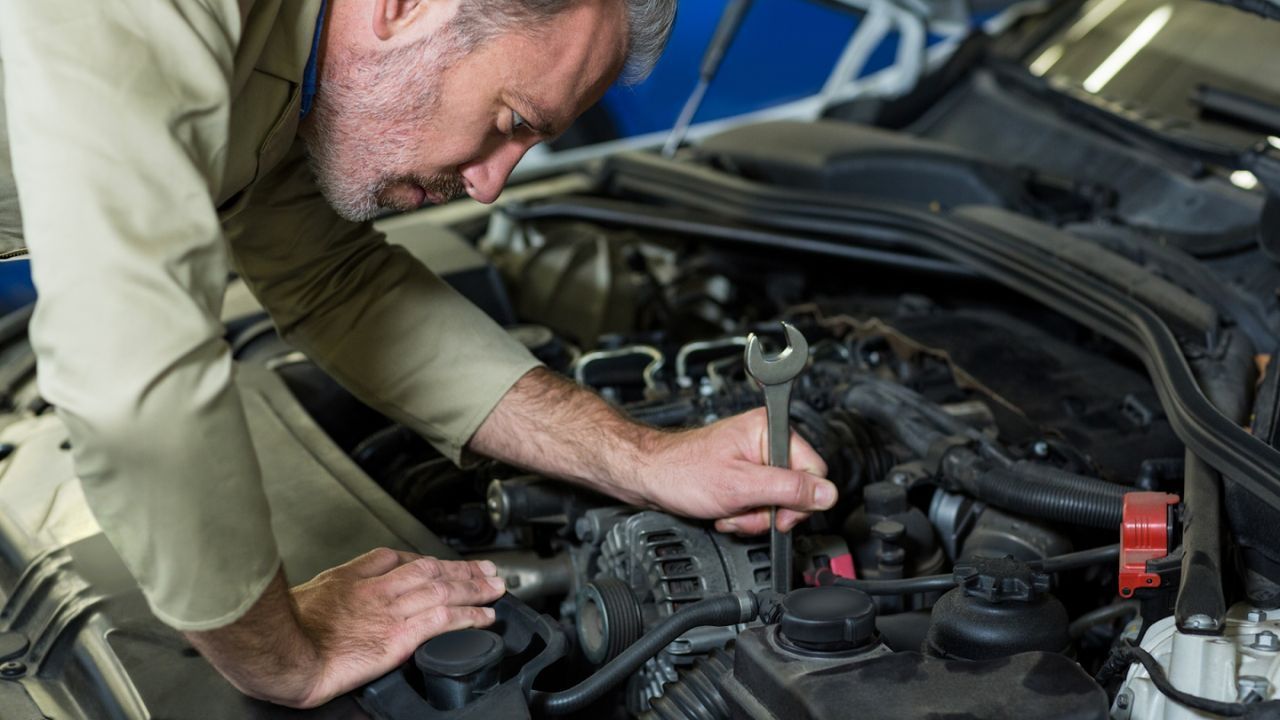 Mechanic working under an open car hood during a vehicle maintenance
