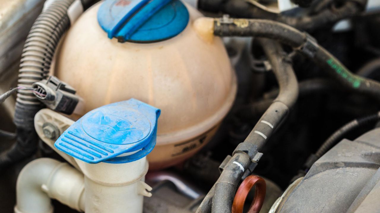 Coolant overflow tank and windshield washer reservoir under a car engine hood
