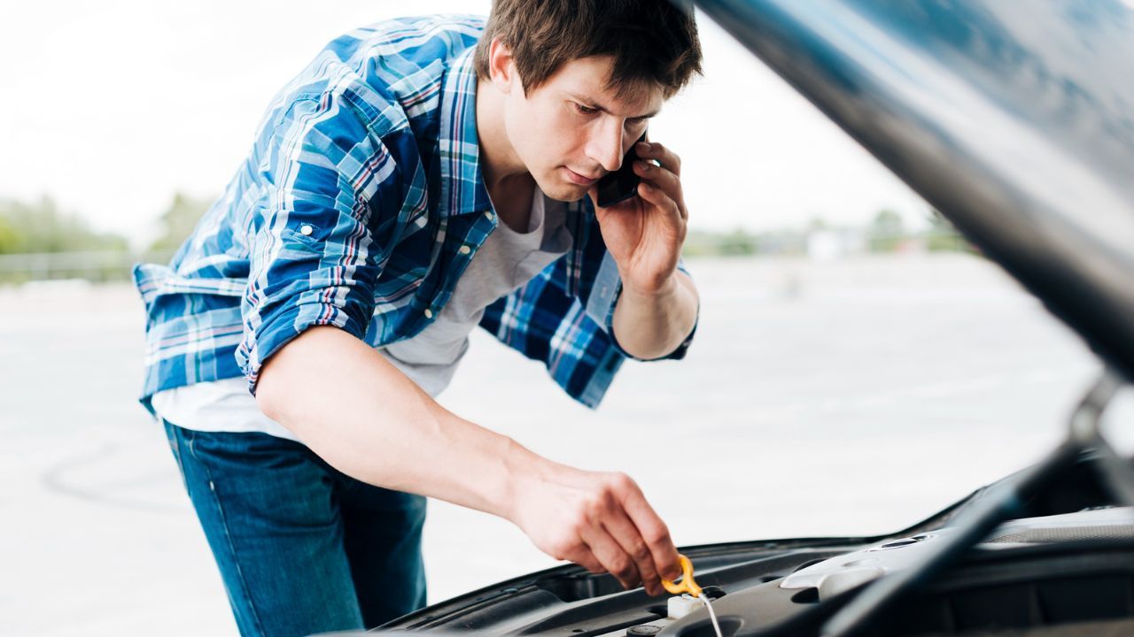 Driver inspecting engine oil levels while speaking with a mechanic on the phone
