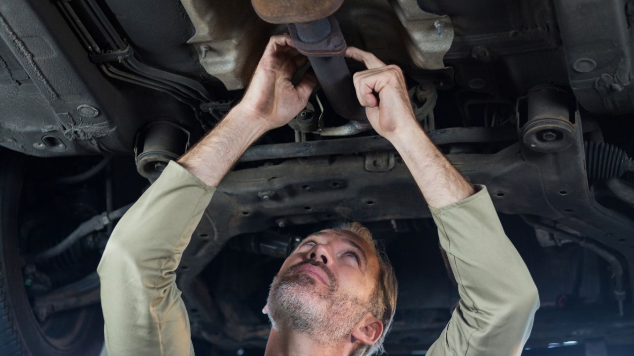 Automotive technician inspecting the exhaust system and muffler underneath a vehicle during a preventive maintenance service.
