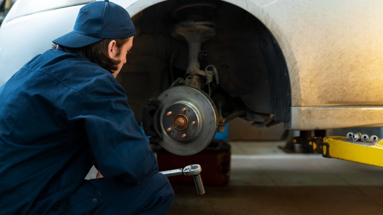 Auto technician inspecting a vehicle’s wheel bearing while it is lifted.
