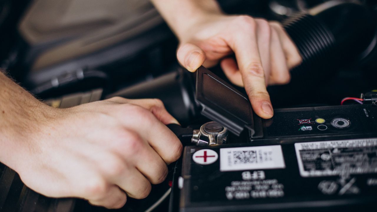 Close-up of a technician loosening a vehicle battery terminal with a wrench before installing a new battery.