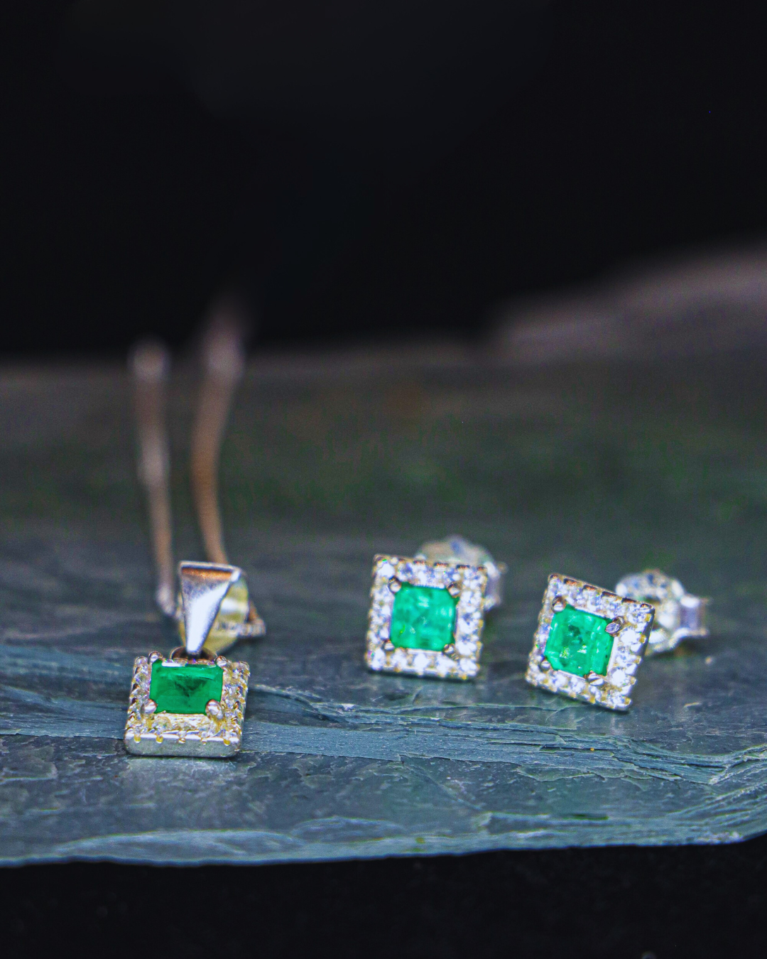 Pendientes con gemas verdes y pendientes pequeños a juego sobre una superficie de piedra texturizada