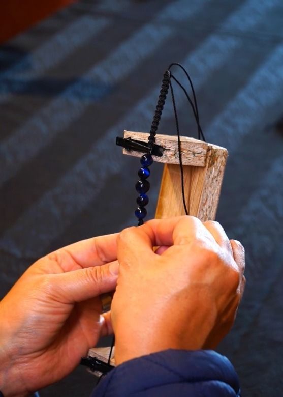 Manos pasando un cordón negro de cuentas por un pequeño telar de madera