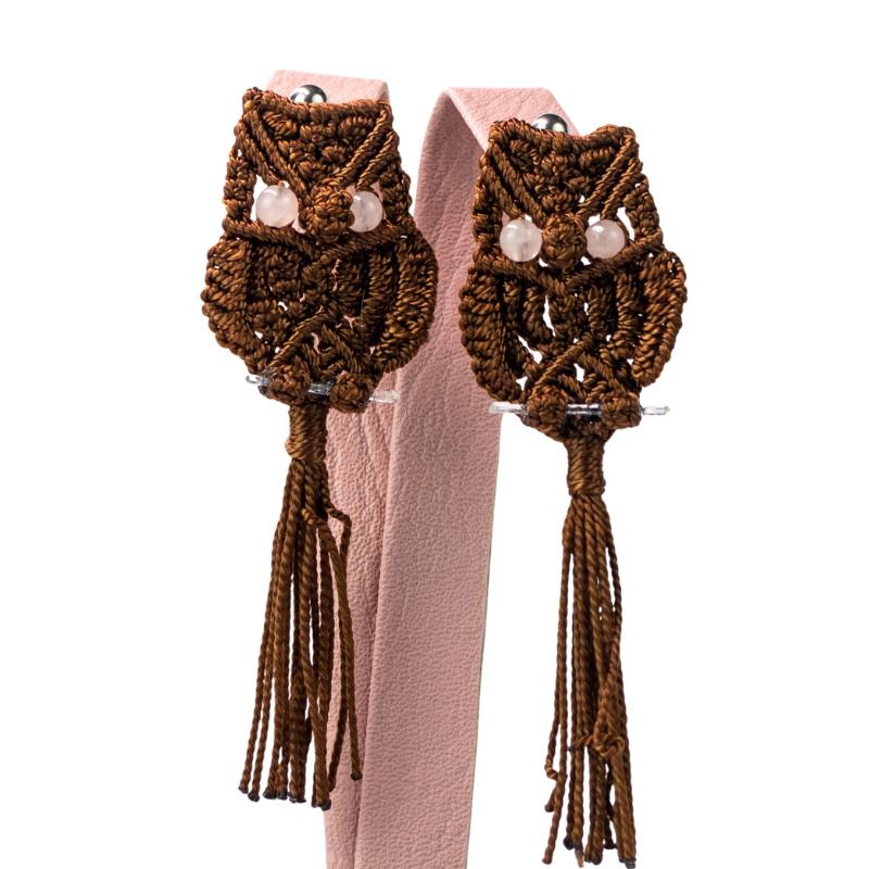 Dos adornos de búho marrones con cuentas y largas borlas, colgados de un soporte rosa