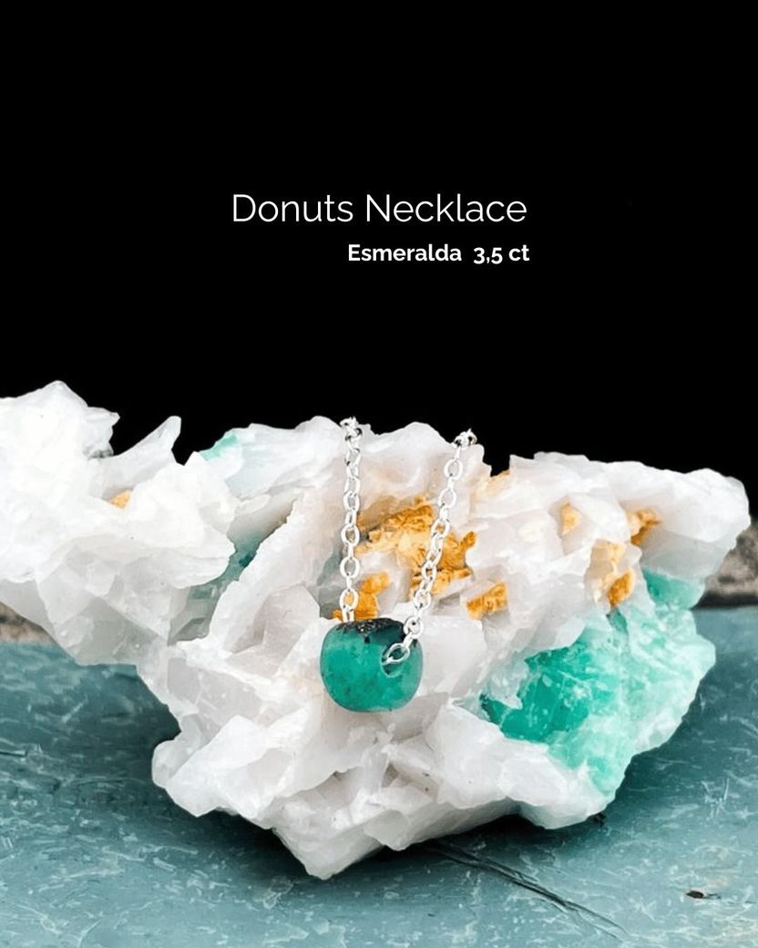 Collar con colgante de donut de esmeralda sobre una roca de cristal.
