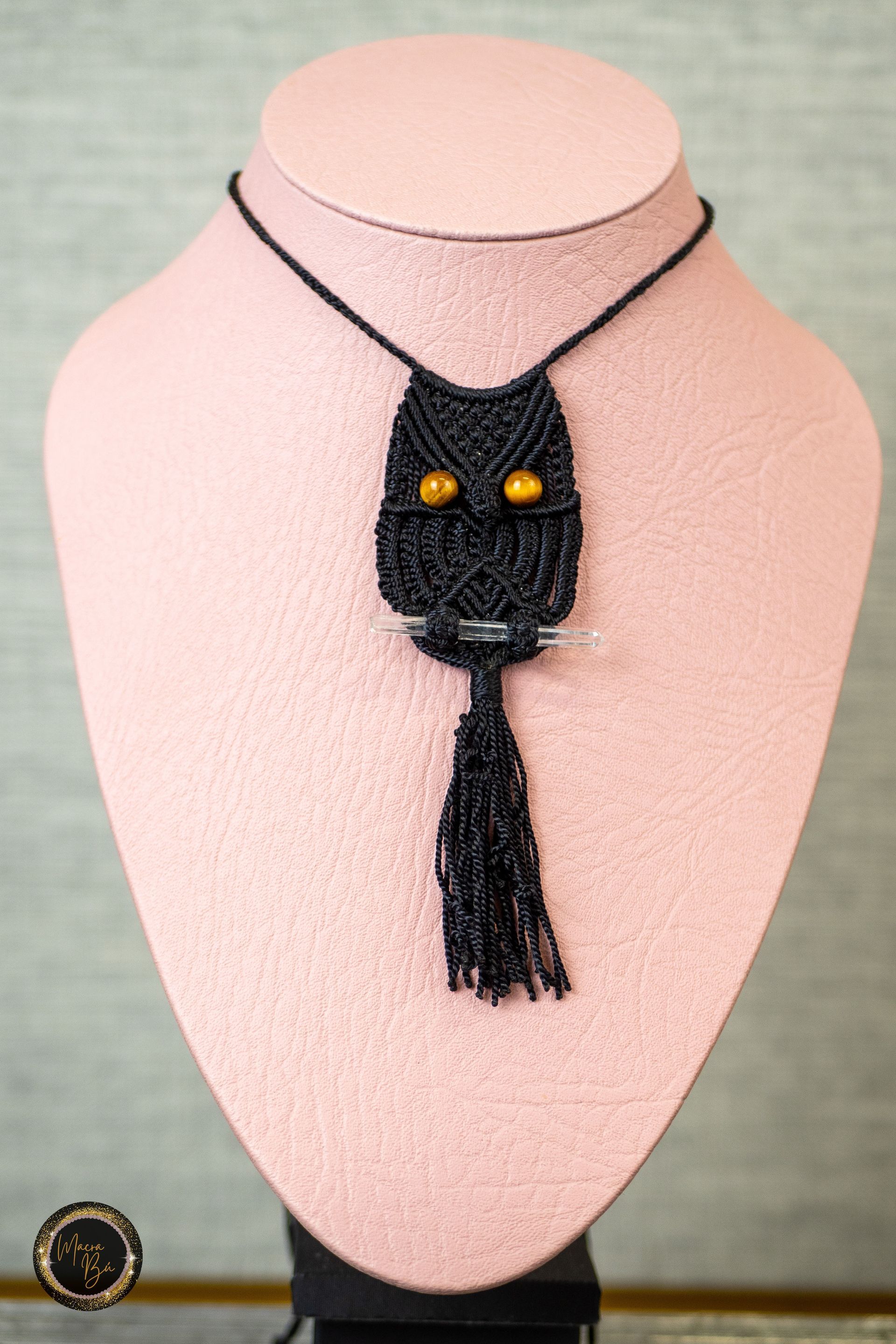 Colgante de búho con cuentas negras y ojos amarillos sobre un busto expositor rosa