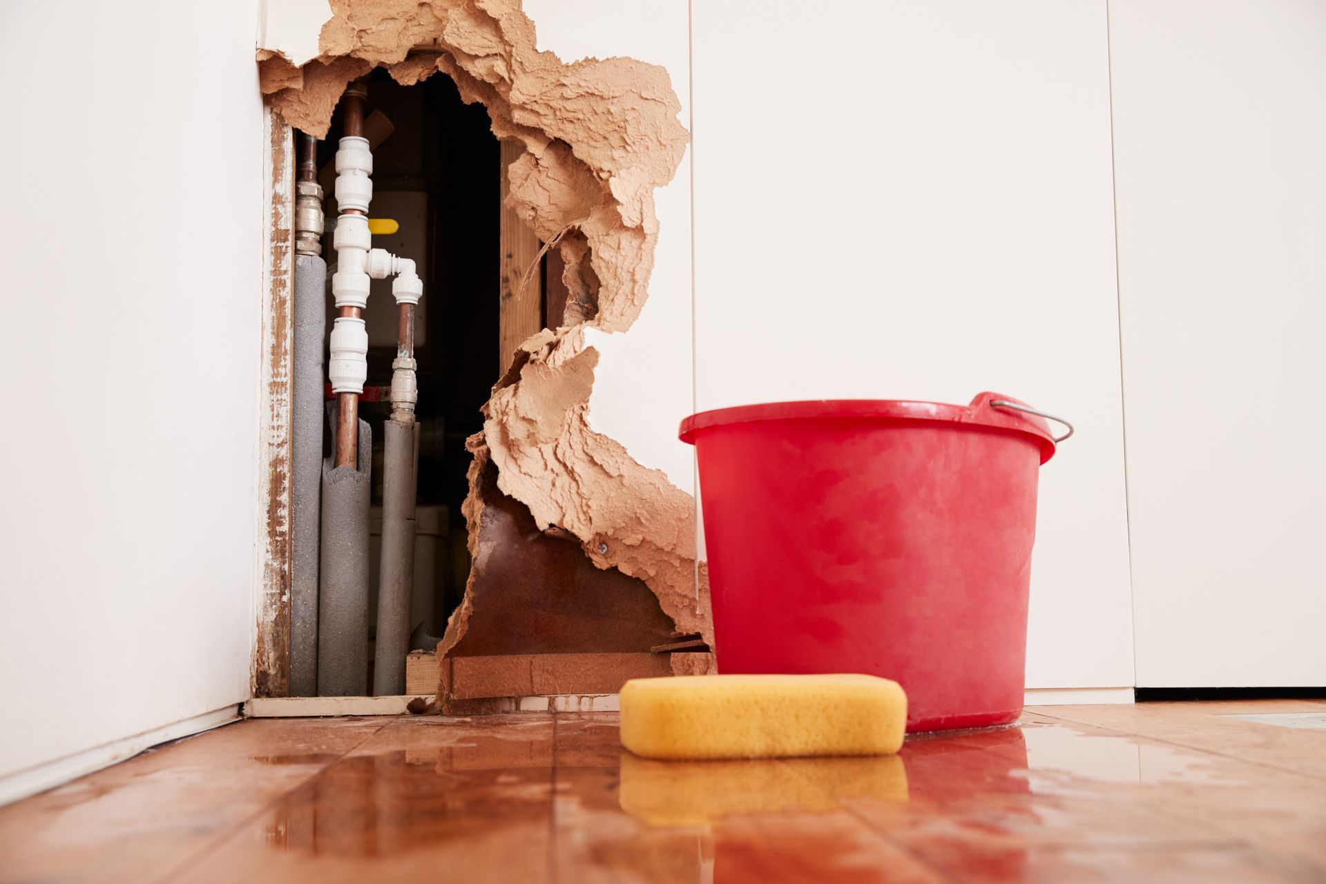Damaged wall, exposed burst water pipes, sponge and bucket.