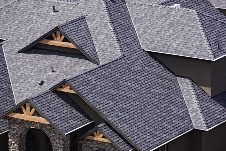 High-angle view of a grey shingled residential roof with multiple gables and decorative wooden accents.