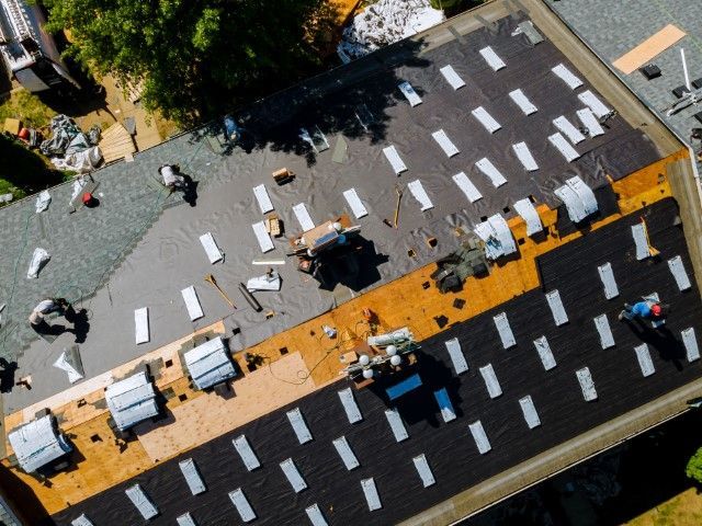An aerial view of a residential roof under repair, showing shingles being removed and replaced by workers.