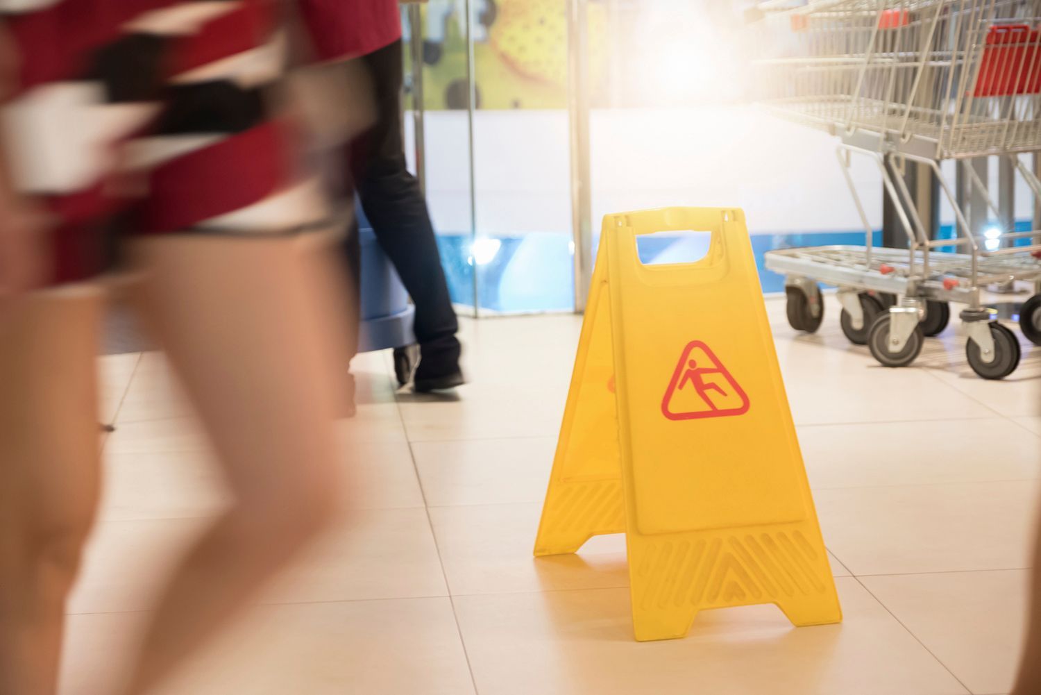 Yellow wet floor sign in a store, with blurry people walking past. Yellow wet floor sign in a store, with blurry people walking past.