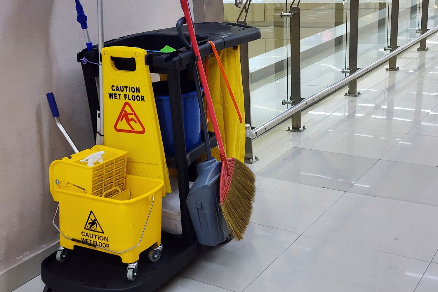 Cleaning cart with wet floor sign and supplies in a hallway.