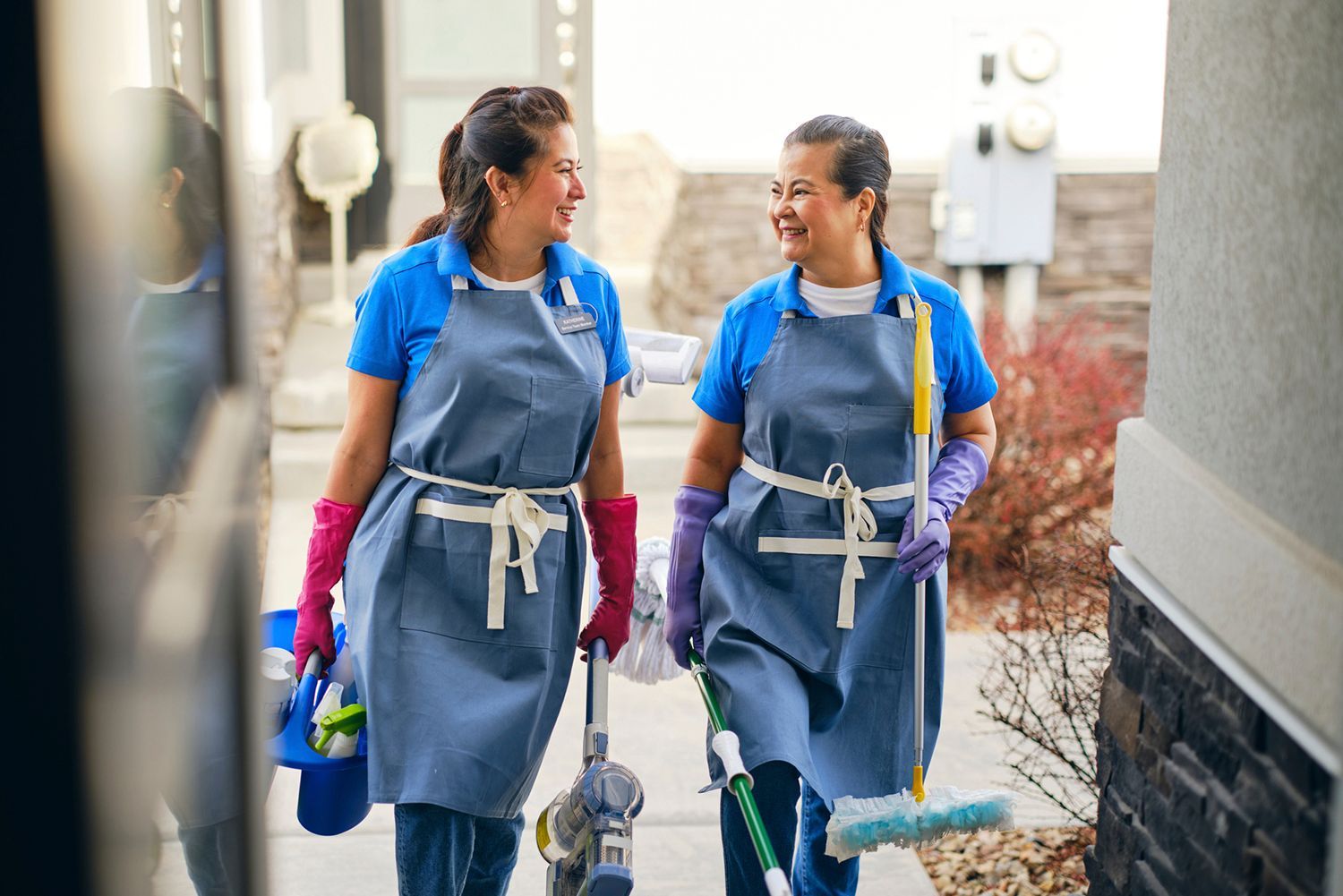 Two cleaning service workers walk together smiling, carrying cleaning supplies. Two cleaning service workers walk together smiling, carrying cleaning supplies.
