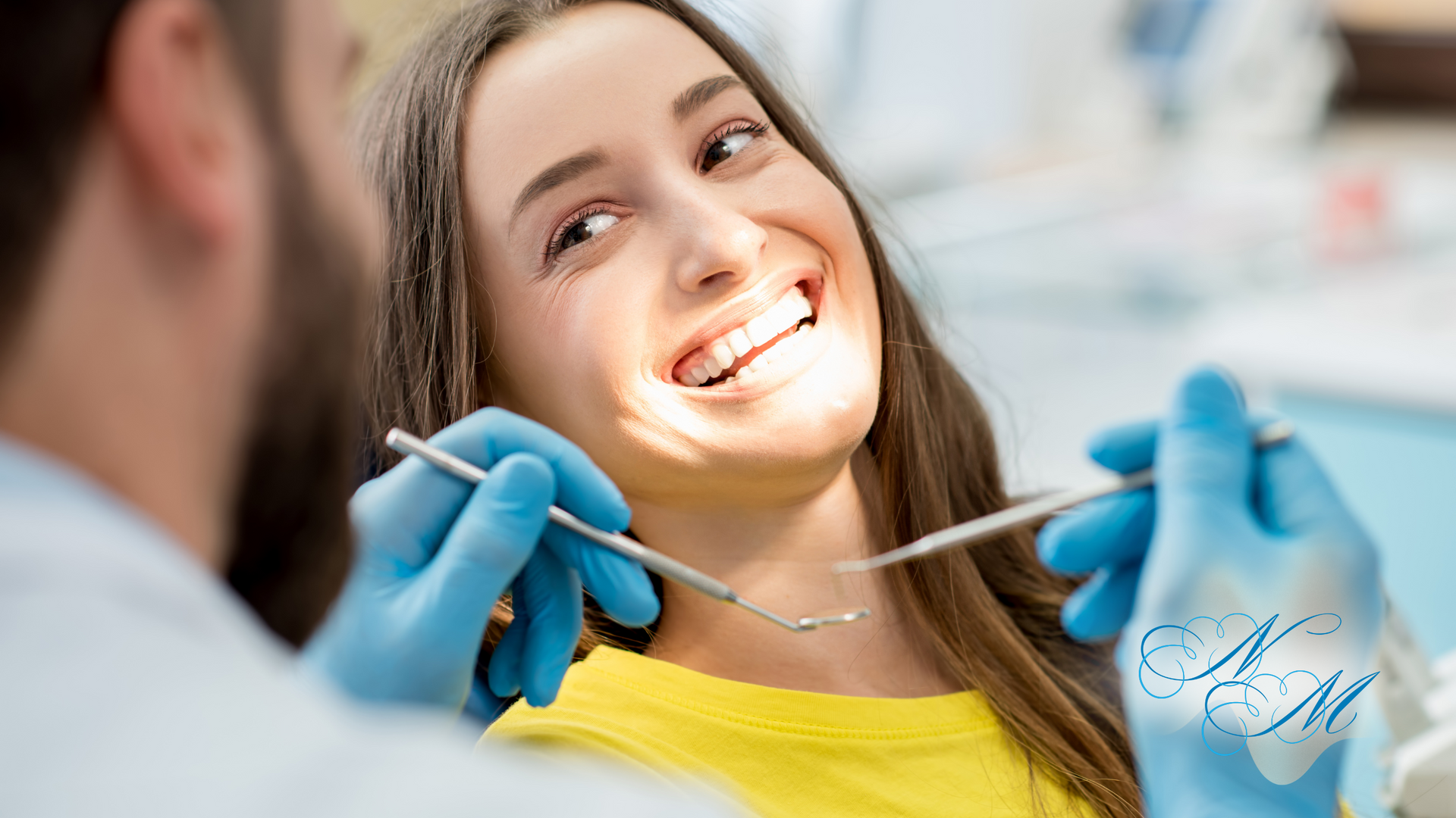 Woman at the dentist smiling, receiving a dental checkup. Dentist holding tools, wearing blue gloves.