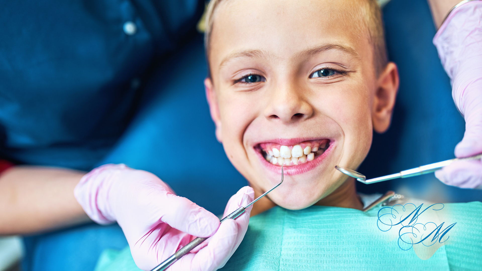 Boy smiling during dental exam; dental tools and gloved hands are visible.