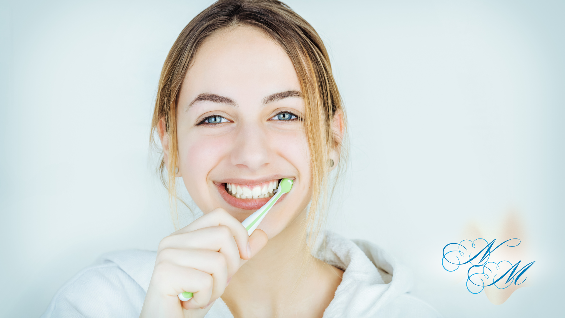 Woman brushing her teeth, smiling broadly, in a bright, white setting.
