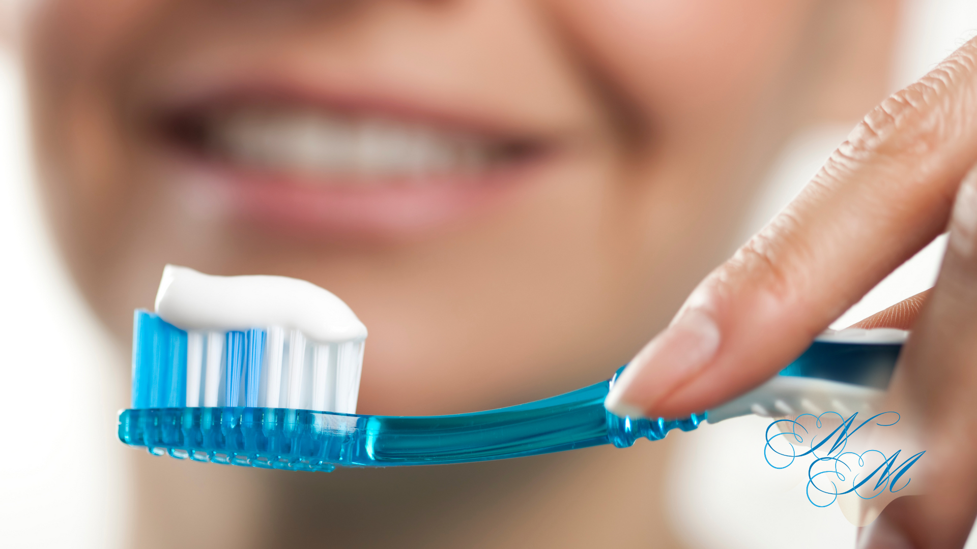 Toothbrush with toothpaste being held near a smiling person.
