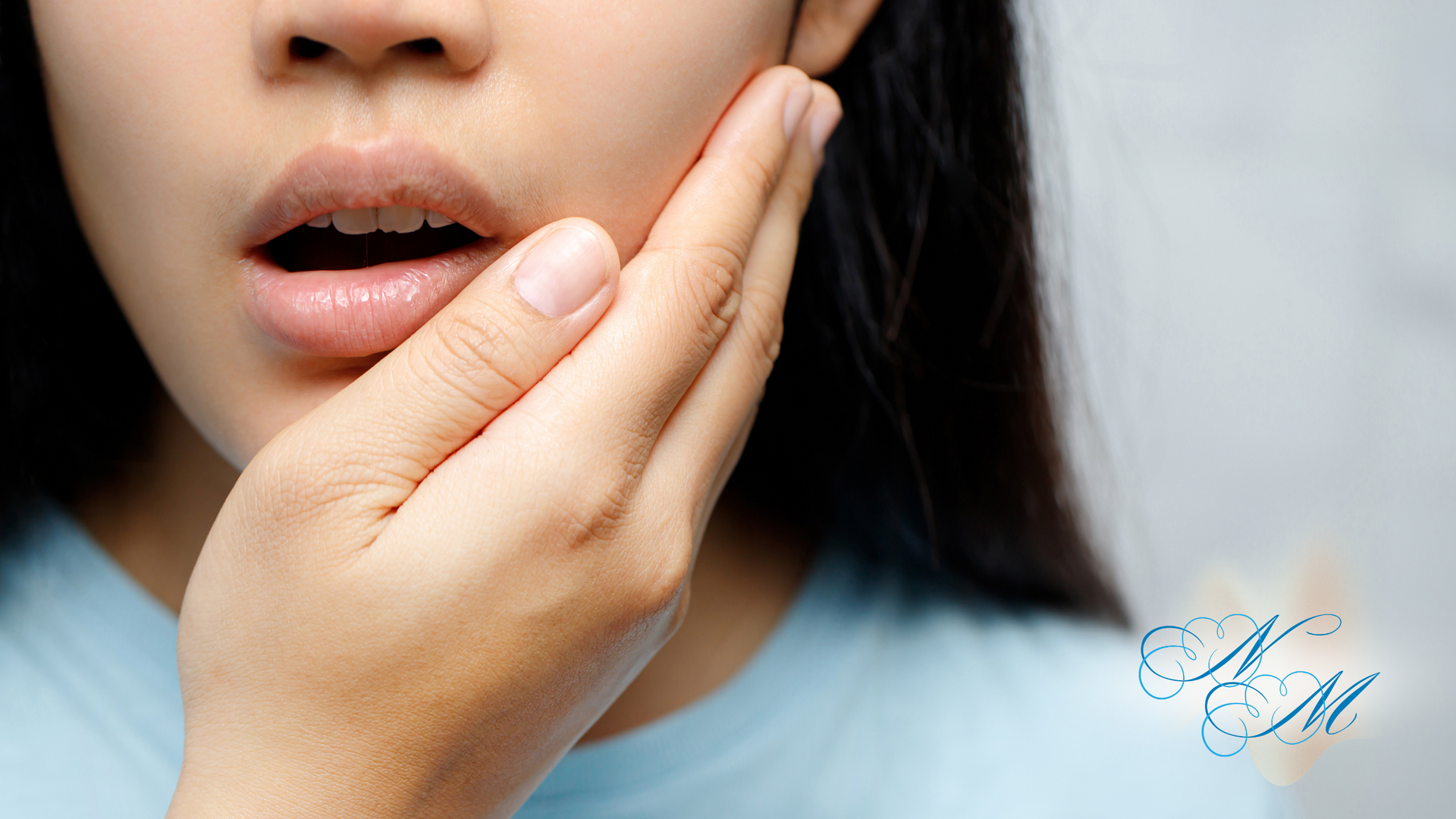 Woman holding her hand to her cheek, mouth slightly open, possibly in pain.