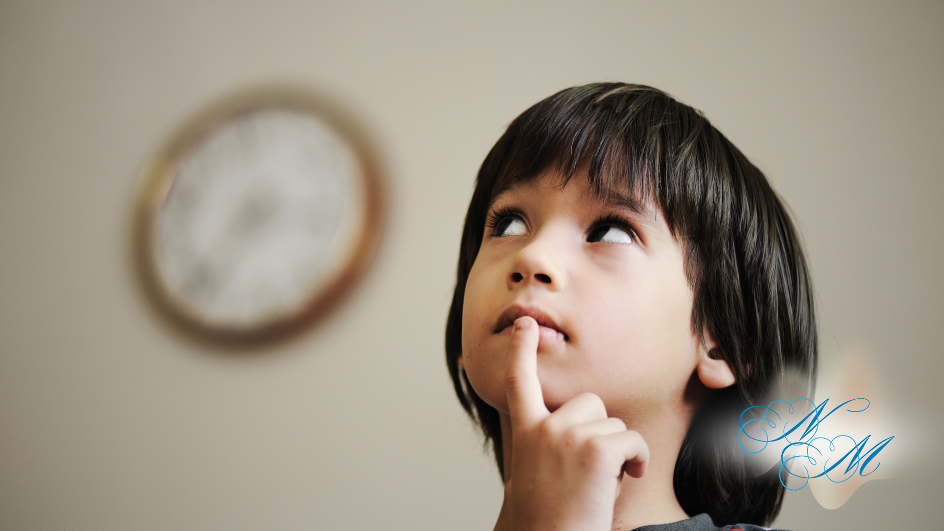 Boy with finger on chin, looking upwards thoughtfully. Clock in the blurred background.