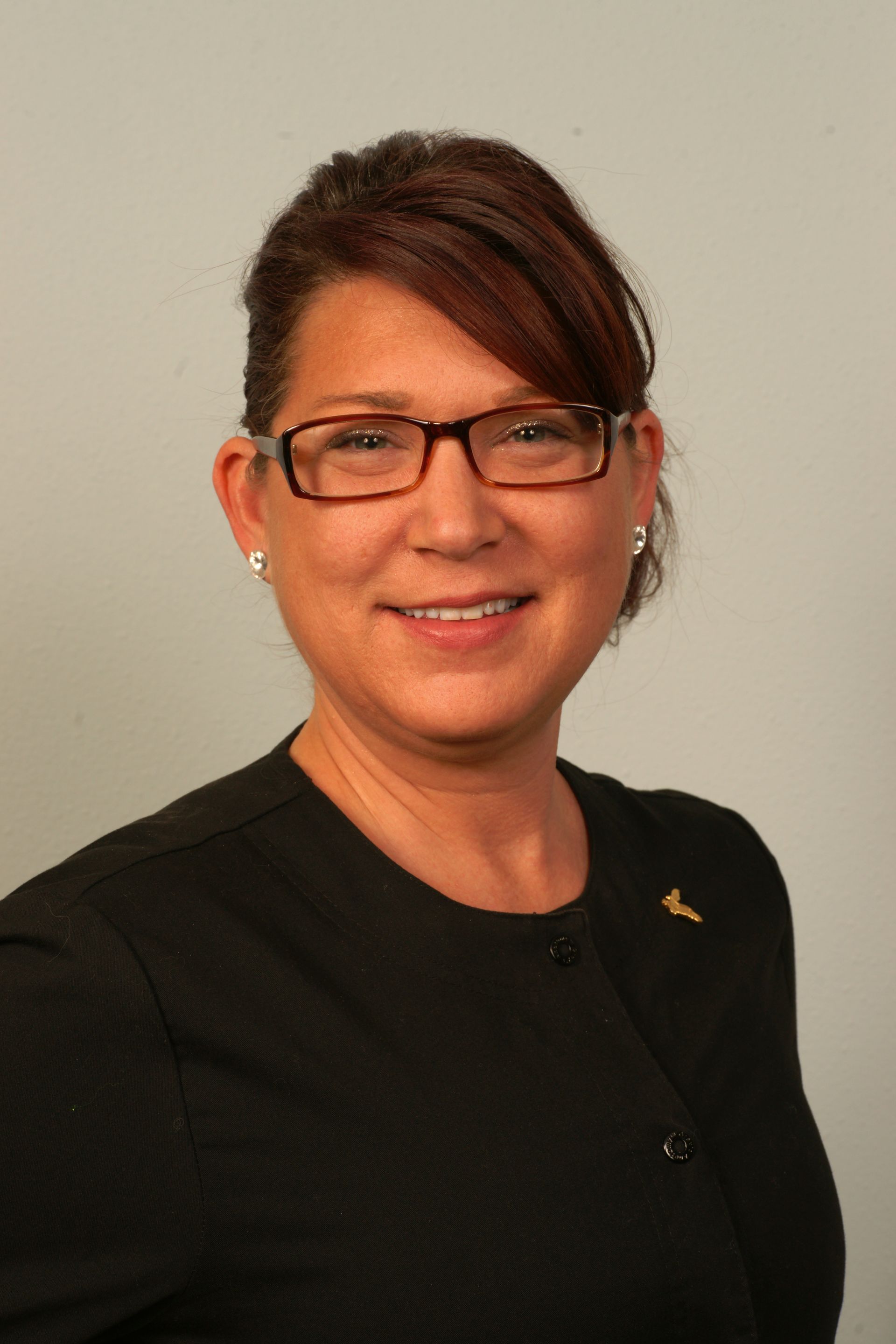 Woman with glasses smiling, wearing black shirt against a gray background.