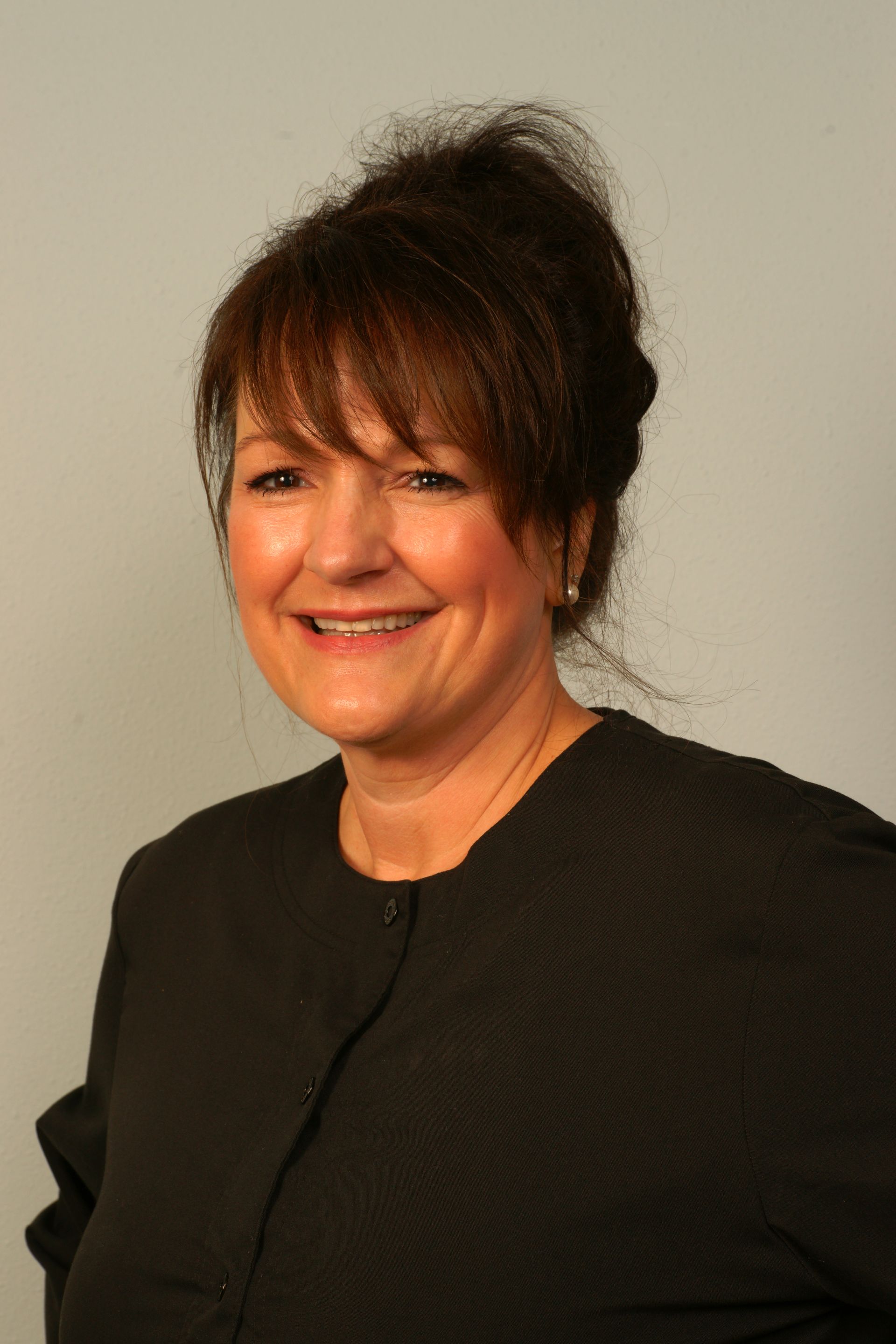 Woman in black top, smiling, looking at the camera against a gray background.
