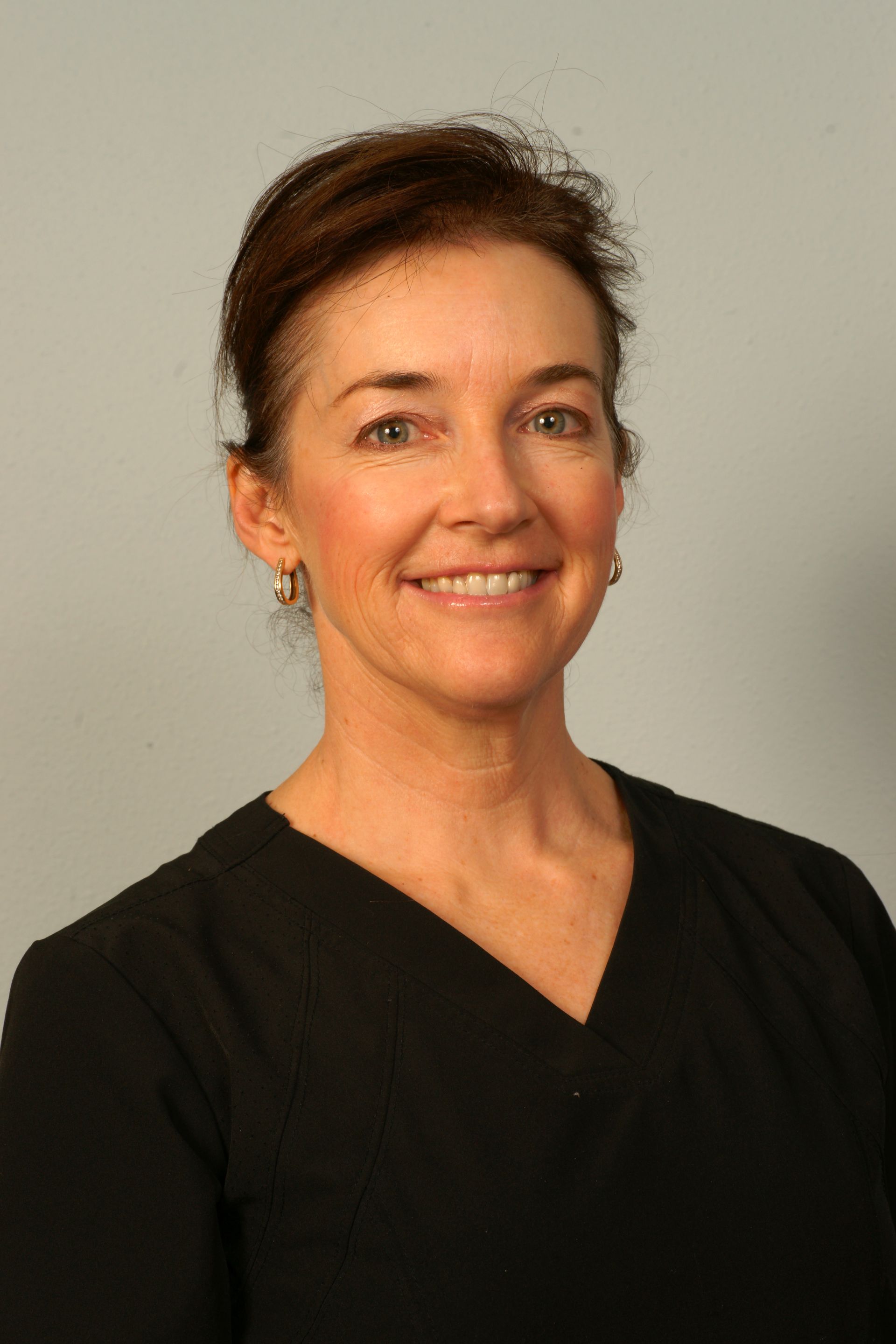 Woman smiling in a black top, against a light gray background.
