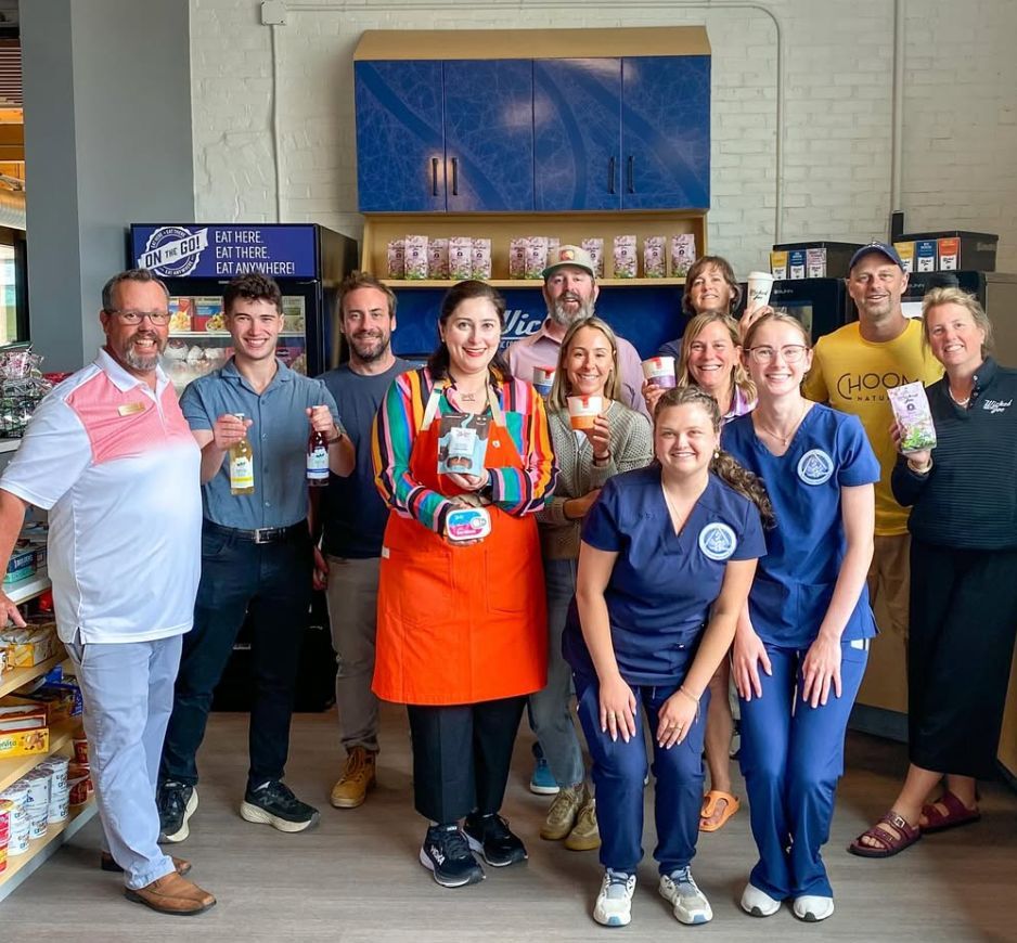 Group of people in a store, smiling and holding products. Blue and orange accents, bright setting.