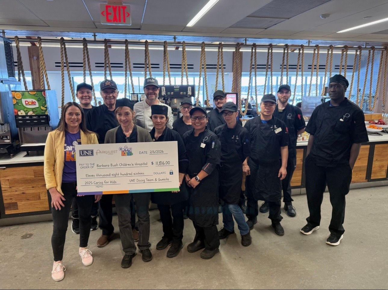 A group of staff members stands together indoors holding a large check.