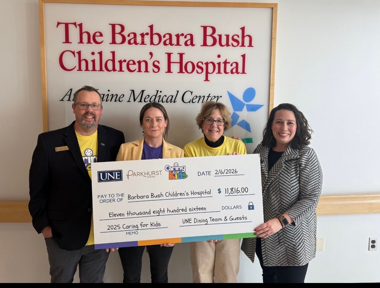 Four people stand in The Barbara Bush Children's Hospital, holding a large check.