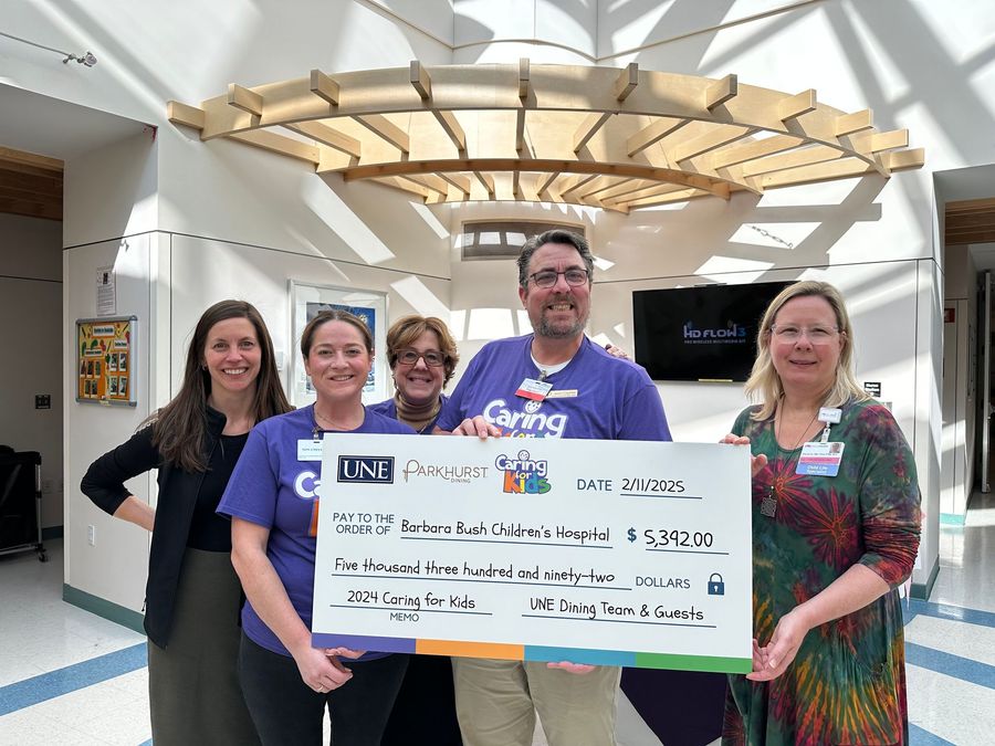 Group of people holding a large check, smiling, indoors. Donation to UNC Children's Hospital.