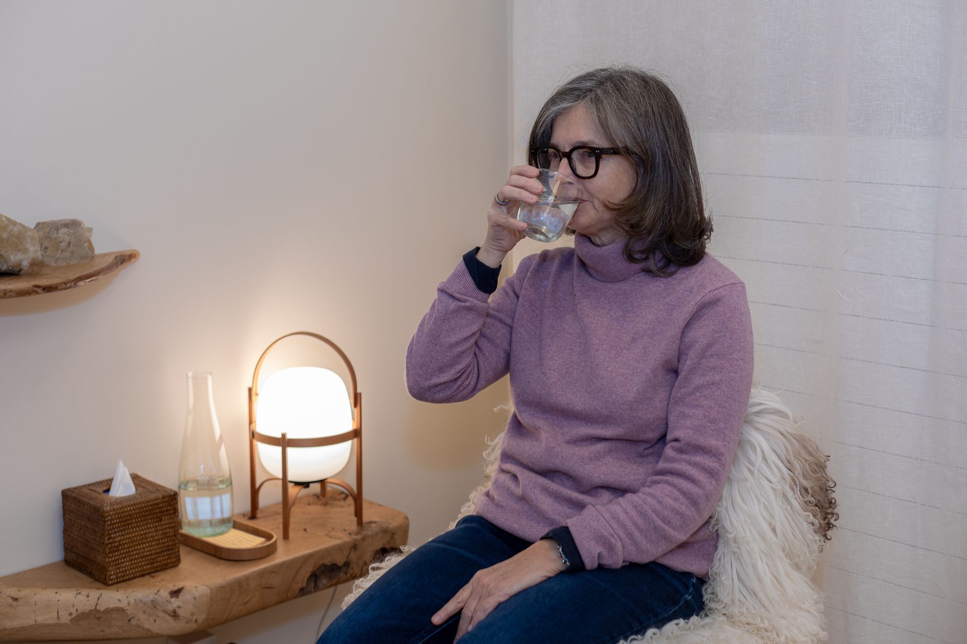 Une femme est assise sur une chaise en train de boire un verre d'eau.