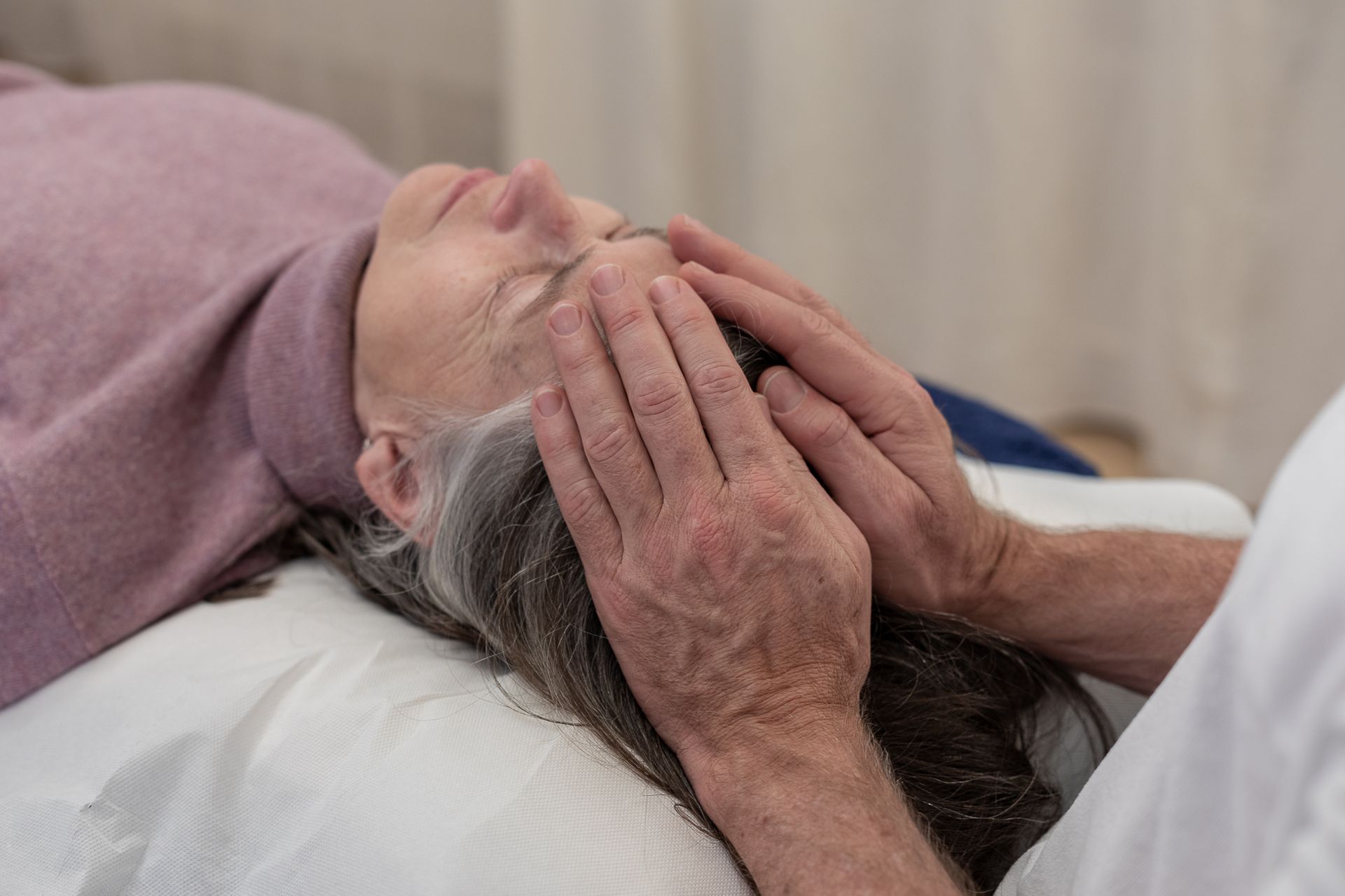 Une femme est allongée sur un lit et reçoit un massage de la tête.