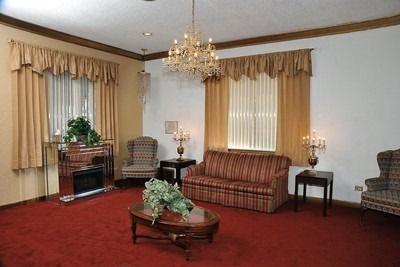 Red-carpeted living room with striped sofa, armchairs, coffee table, lamps, and chandeliers