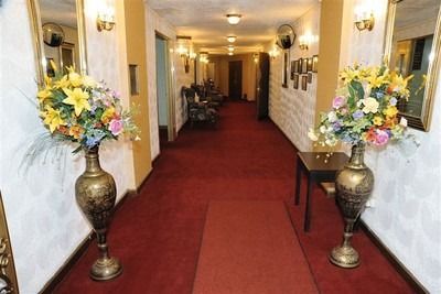 Elegant hotel hallway with red carpet, white walls, and tall floral arrangements by the entrance.