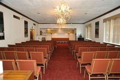 Small chapel interior with rows of red chairs facing an altar under a chandelier
