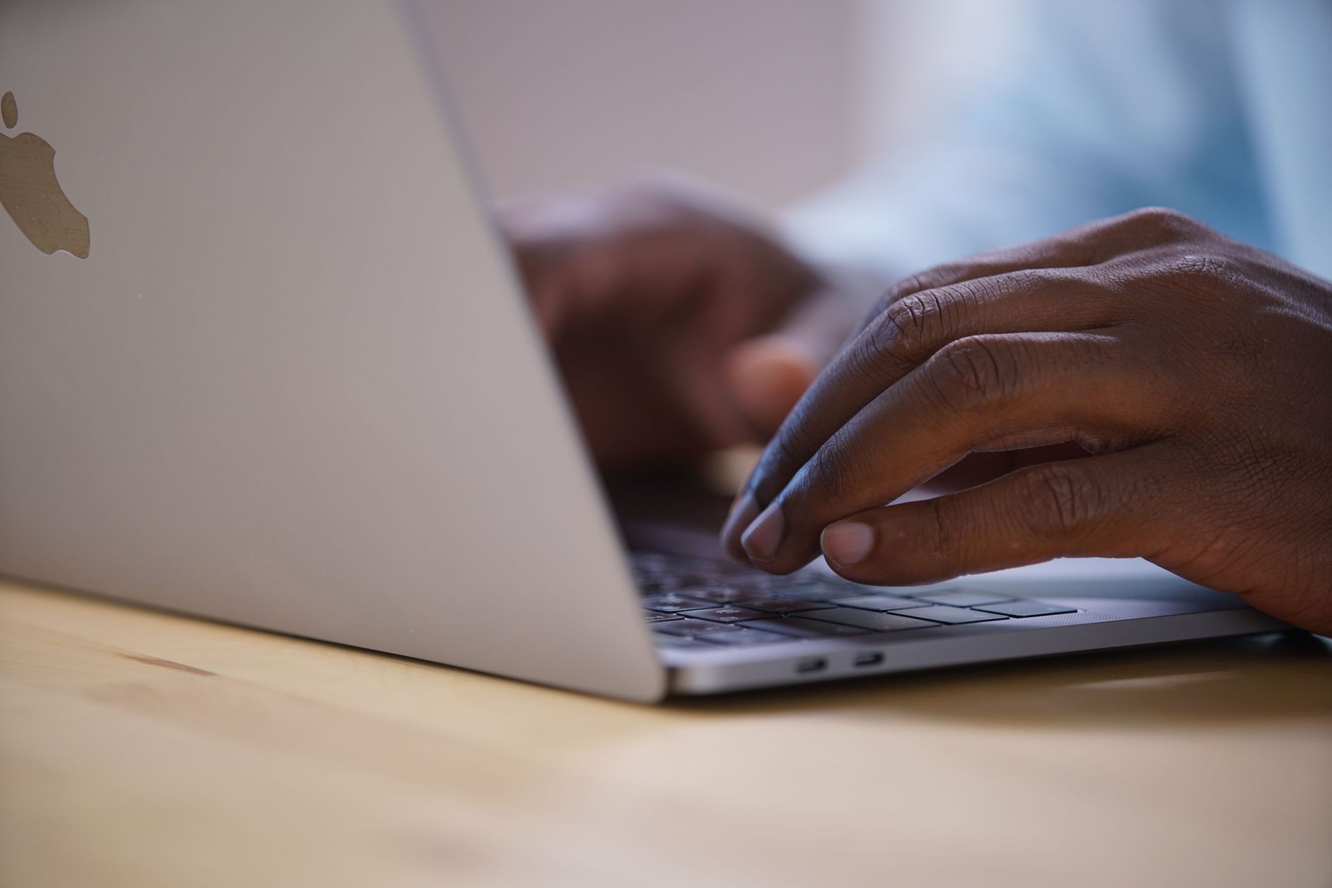 Hands typing on a laptop keyboard beside a dark notebook on a white desk