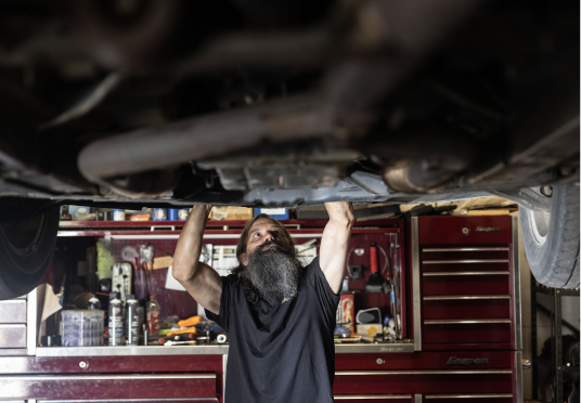Mechanic working under a raised car in a red tool cabinet garage | Endurance Auto Repair and Tire