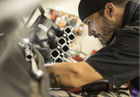 Mechanic in black shirt and cap working on an engine with tools in a workshop | Endurance Auto Repair and Tire