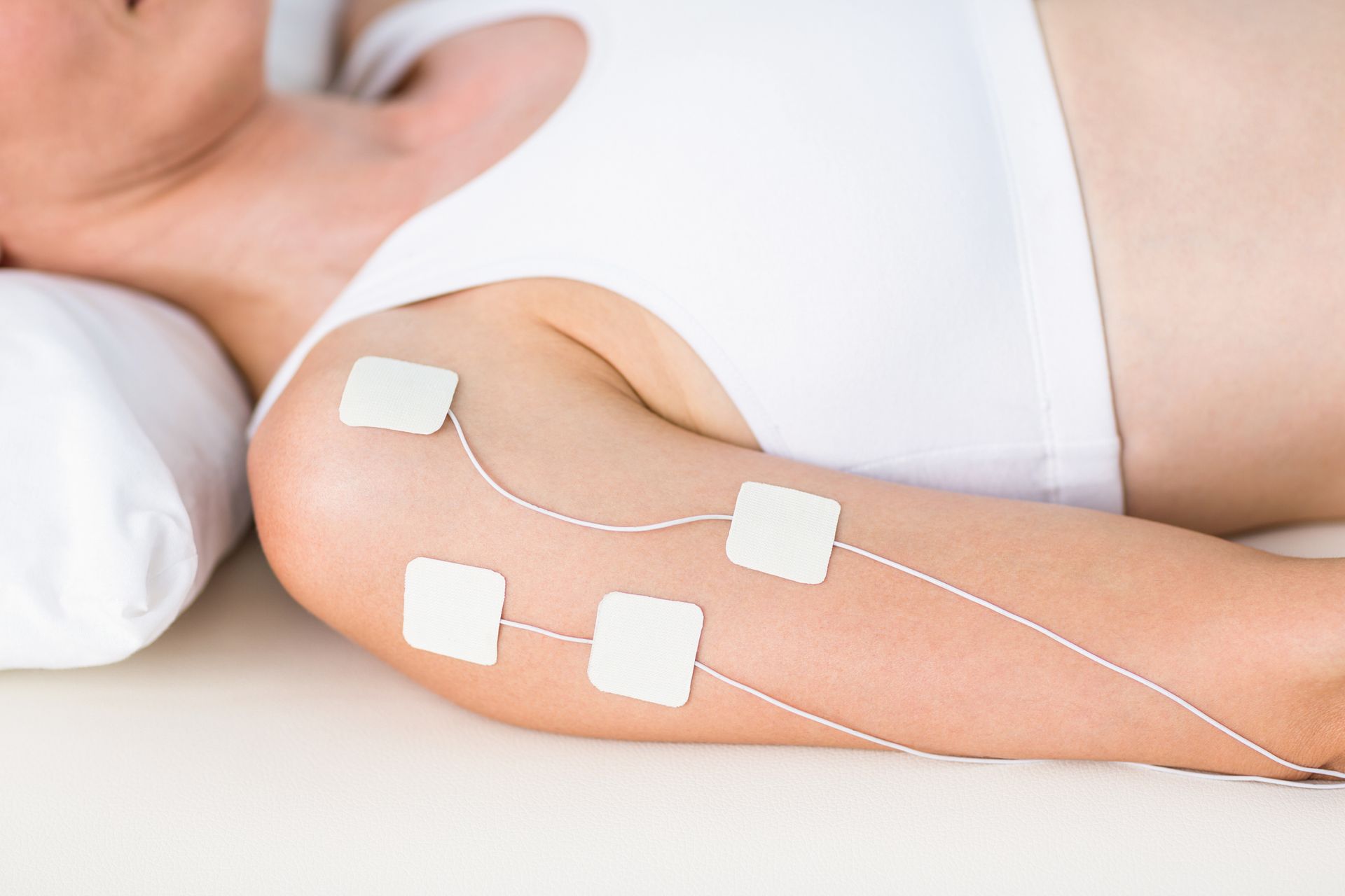 A woman is laying on a bed with electrodes on her arm.