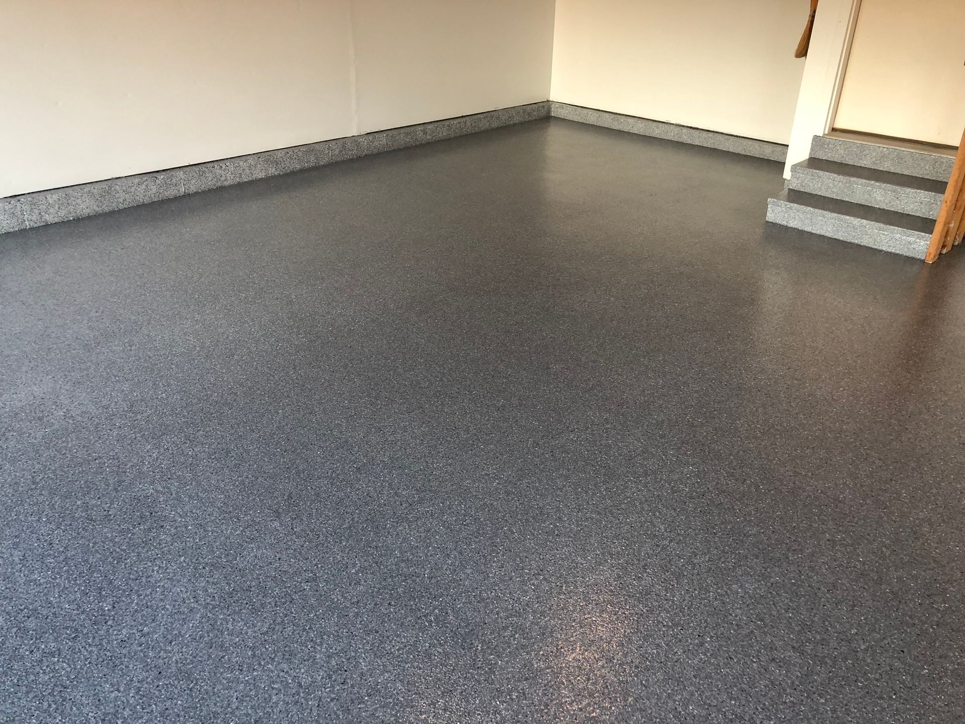 Empty garage with gray speckled floor, beige walls, and a small staircase on the right.