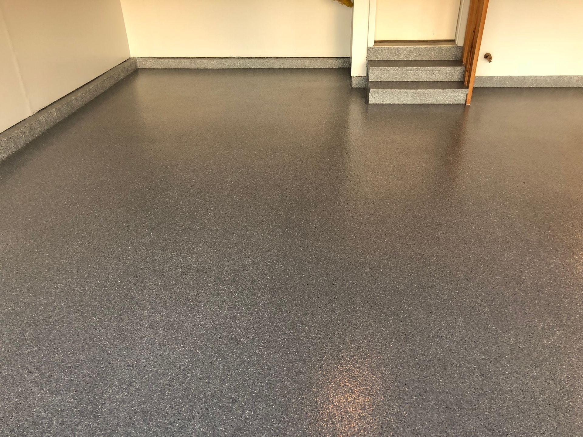 Empty garage with speckled gray floor and steps leading to a doorway at the back